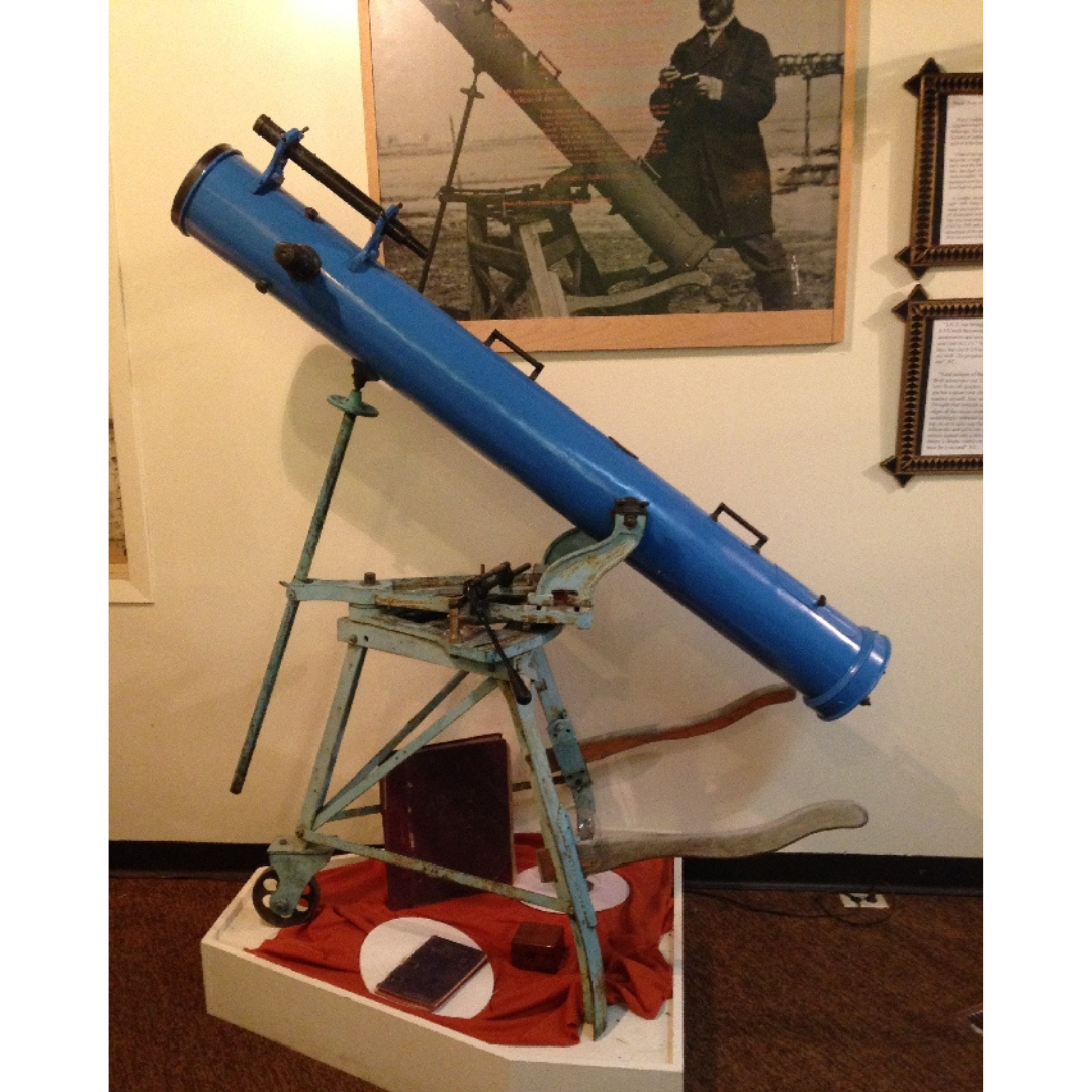 A blue telescope on display on a small pedestal in a museum.