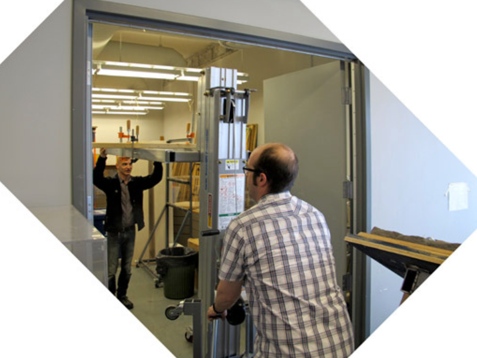 A photo showing two individuals navigating a drywall lift through a doorway.