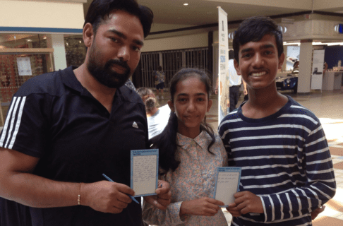 Three young people pose for a photo holding up activity cards from a museum pop-up in a shopping centre.