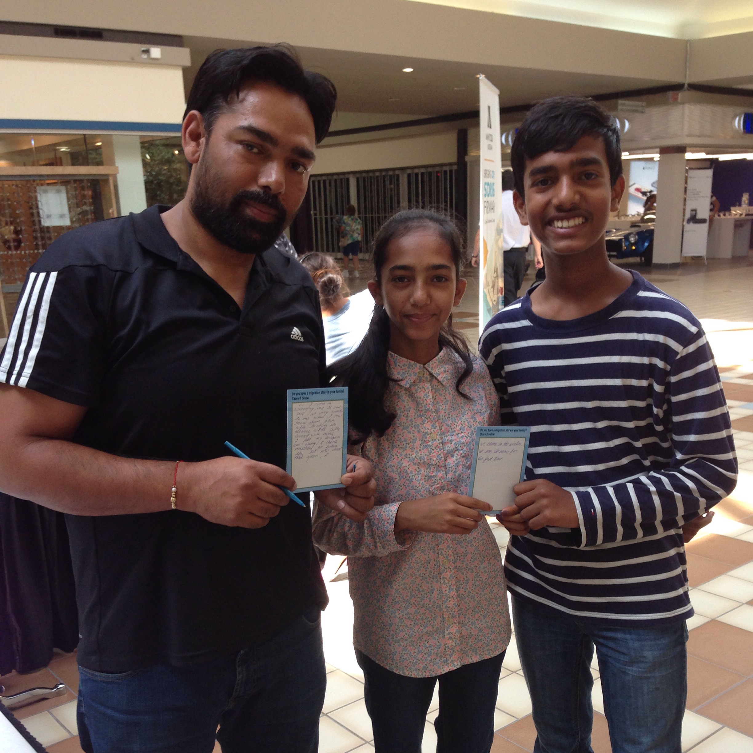 Three young people pose for a photo holding up activity cards from a museum pop-up in a shopping centre.