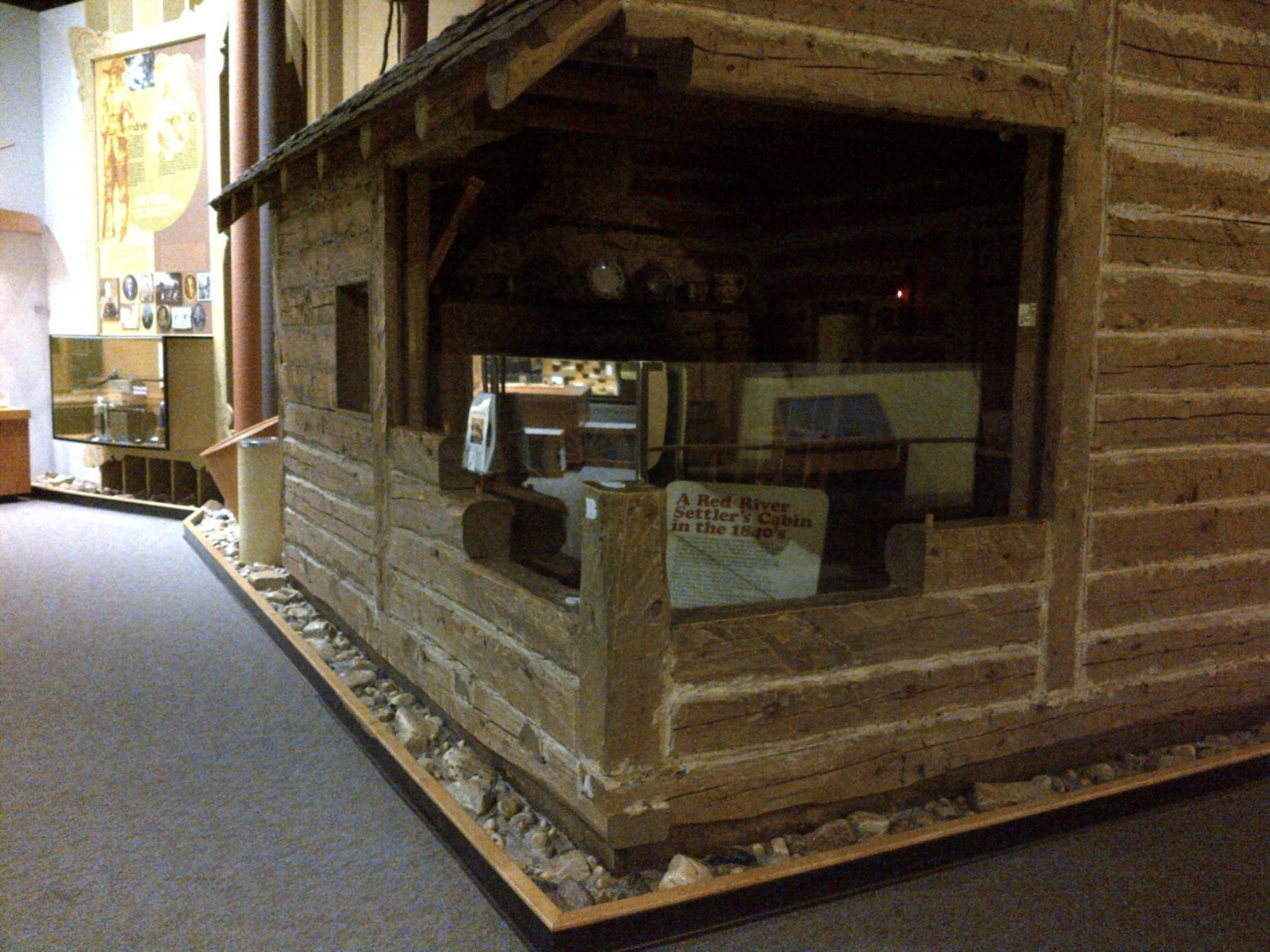 A log cabin in the Grasslands Gallery, with the close corner "cut out" to reveal inside the cabin. Inside is dimly lit and from this distance, not much detail can be seen.