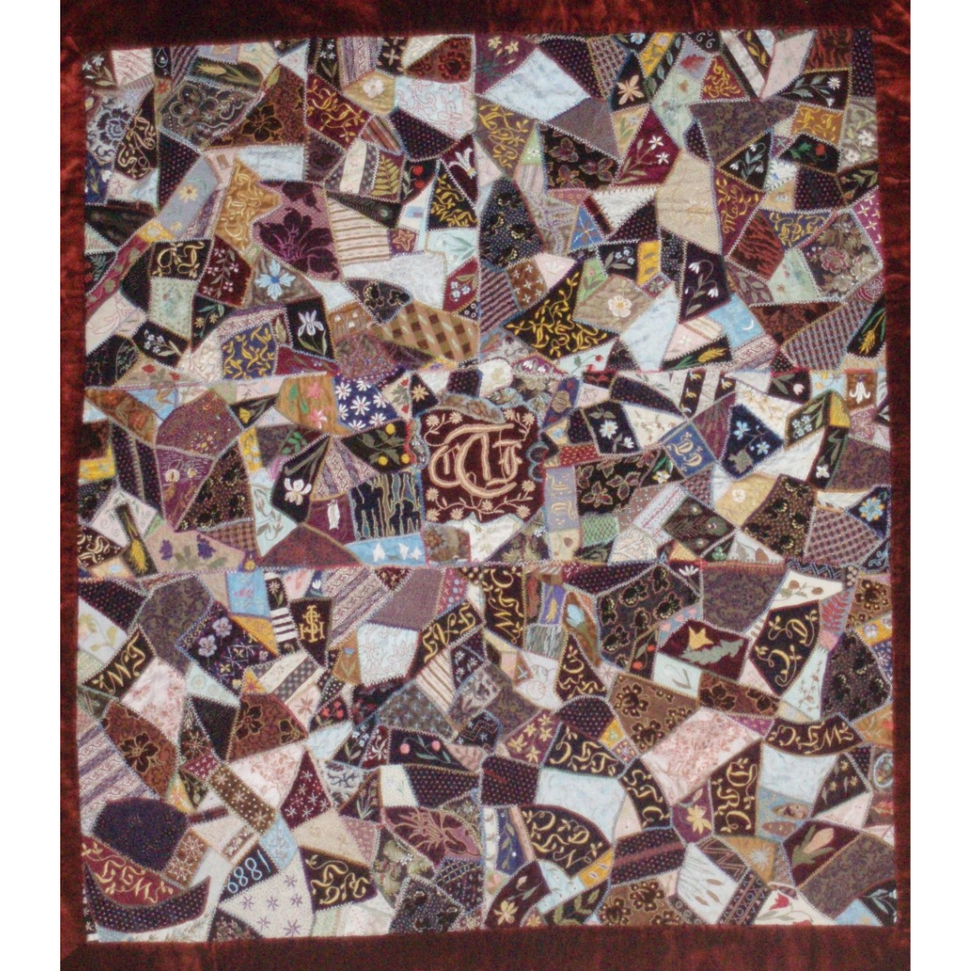 A patchwork quilt made from patches of varying shapes in browns, reds, creams, blues, blacks, and yellows.