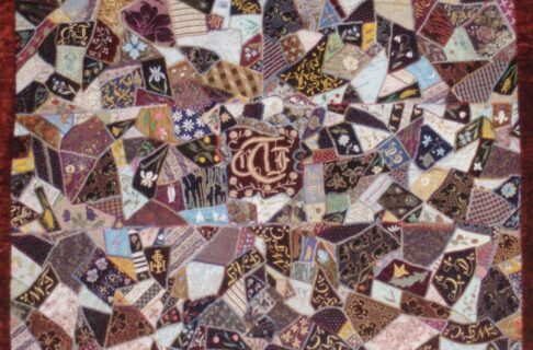 A patchwork quilt made from patches of varying shapes in browns, creams, blues, blacks, and yellows.