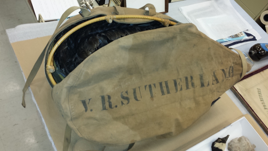 A canvas bag unzipped along the centre, with a rounded cane frame inside allowing for storage of the decoy components. Stamped on the bottom of the bag is "V. R. Sutherland".