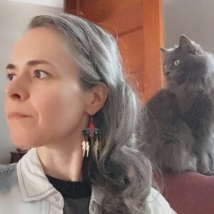 Informal headshot of Alexis Miller in profile, looking to the left alongside a grey cat perched on the back of her chair.