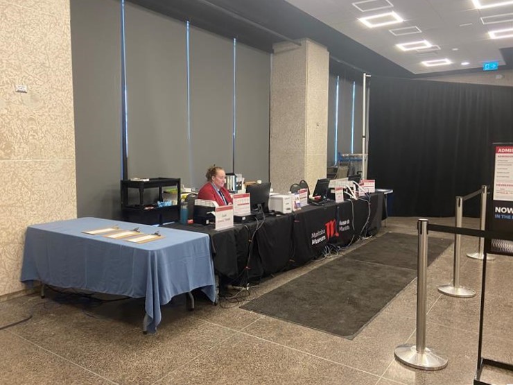 A temporary Box Office set up in a large room, with tables laid with Manitoba Museum branded tablecloths and computers in front of a designated space for a queue.