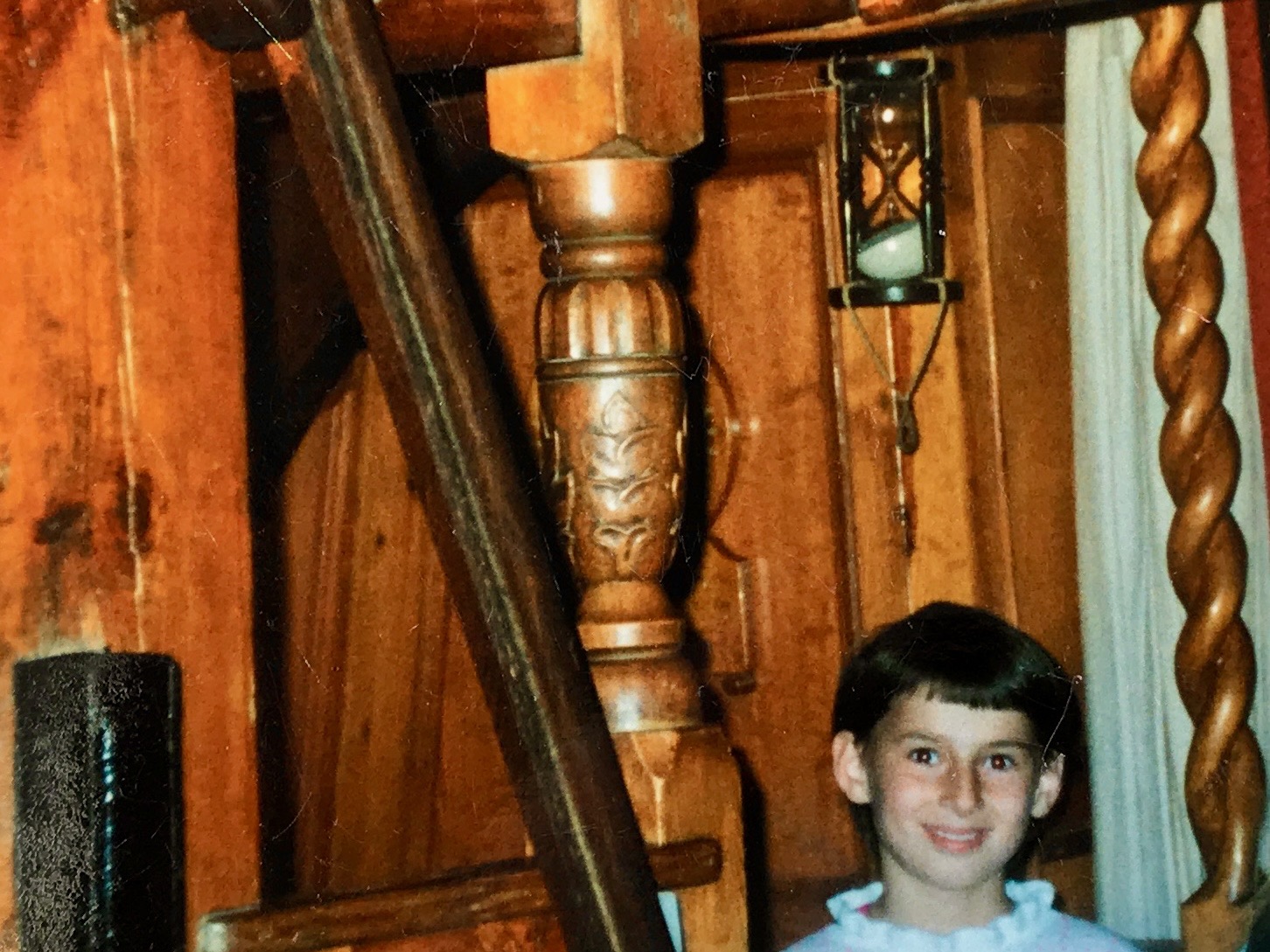 A smiling child sitting in the interior of the Nonsuch, a wooden sailing vessel.