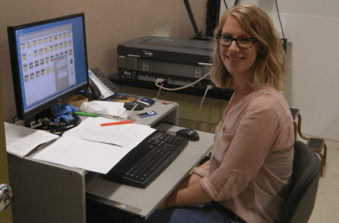 Summer student Jenna smiles towards the camera from her seat at a desk and computer.