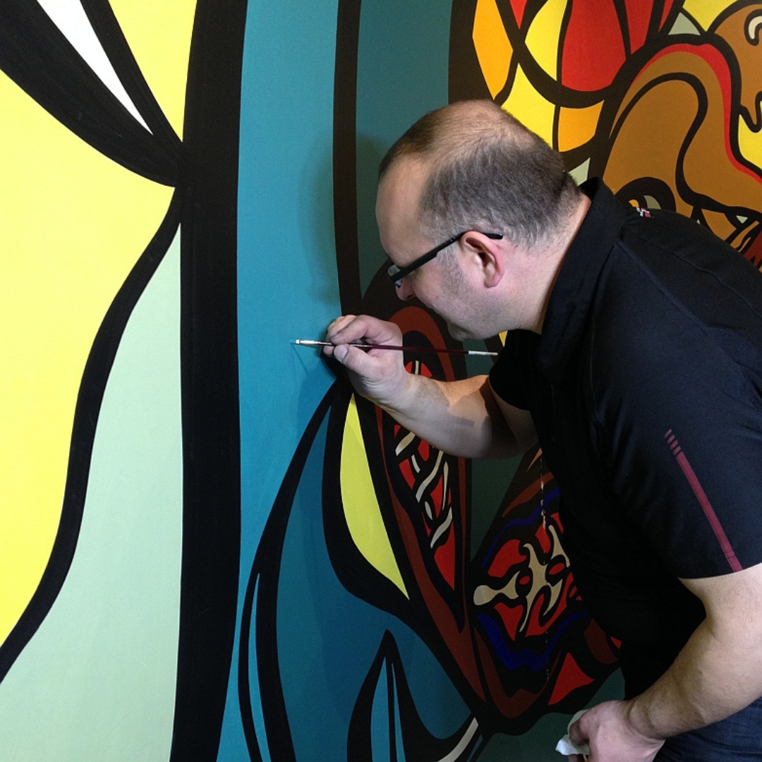 A person painting a very small test spot on a portion of medium blue on the mural.