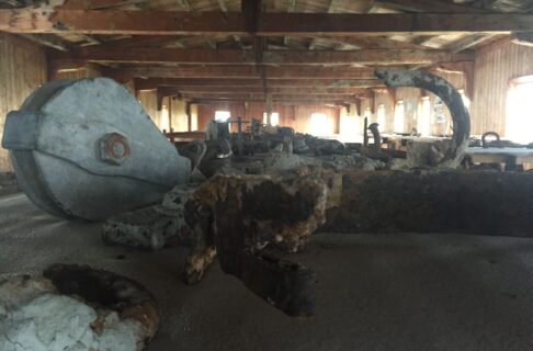 Close up view of a number of artifacts laid out on a table in a long room with wooden walls and a peaked wooden roof. Sunlight streams in at the far end of the room.