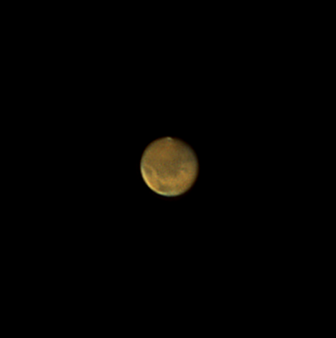 The red planet Mars shows a tiny white polar ice cap at top, and dark markings on its rusty red plains.