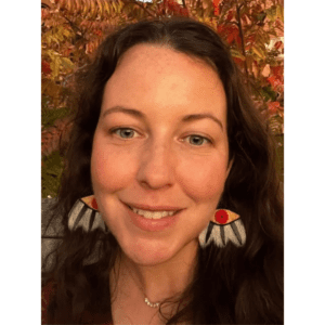 Selfie of a smiling woman with long dark hair, wearing colourful beaded earrings.