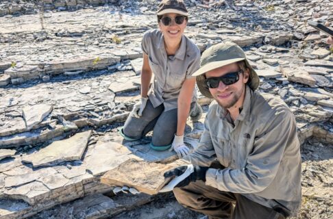 Dr. Joe Moysuik and a coleague on a rocky outcropping holding up a recently found fossil specimen.