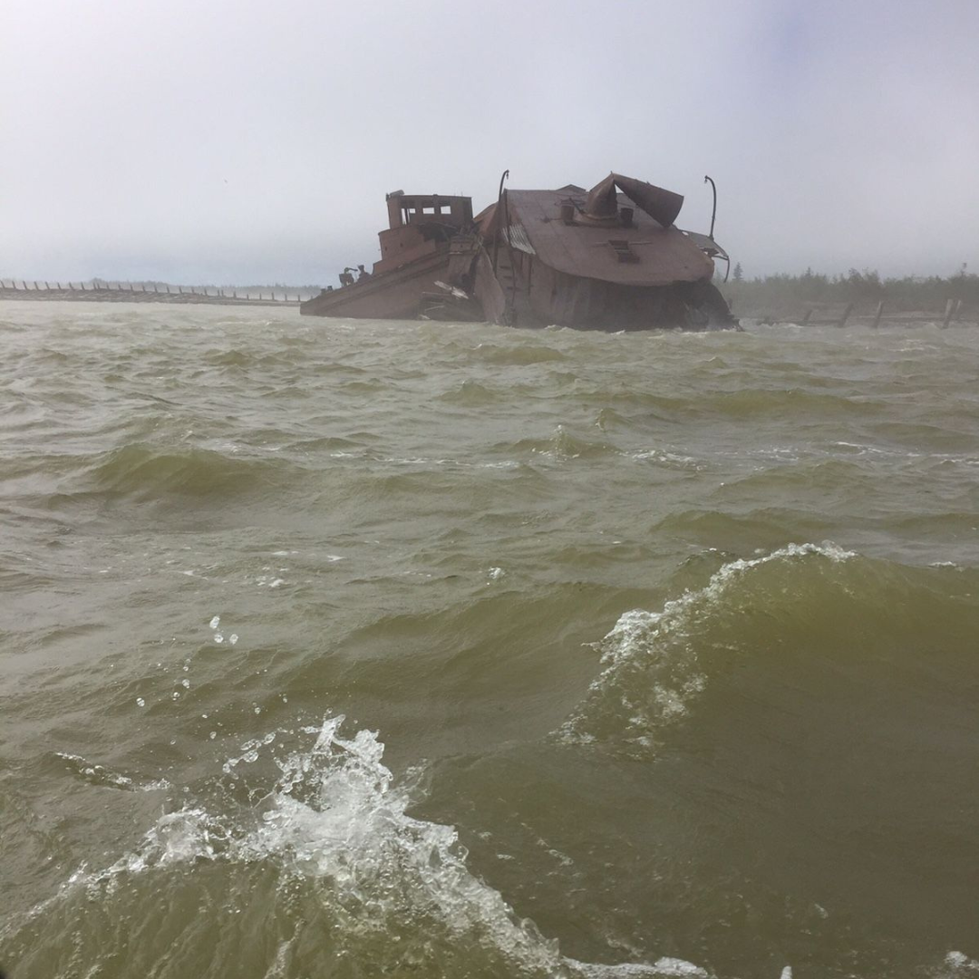 Part of a wrecked dredging ship emerging from choppy water beneath a grey sky.