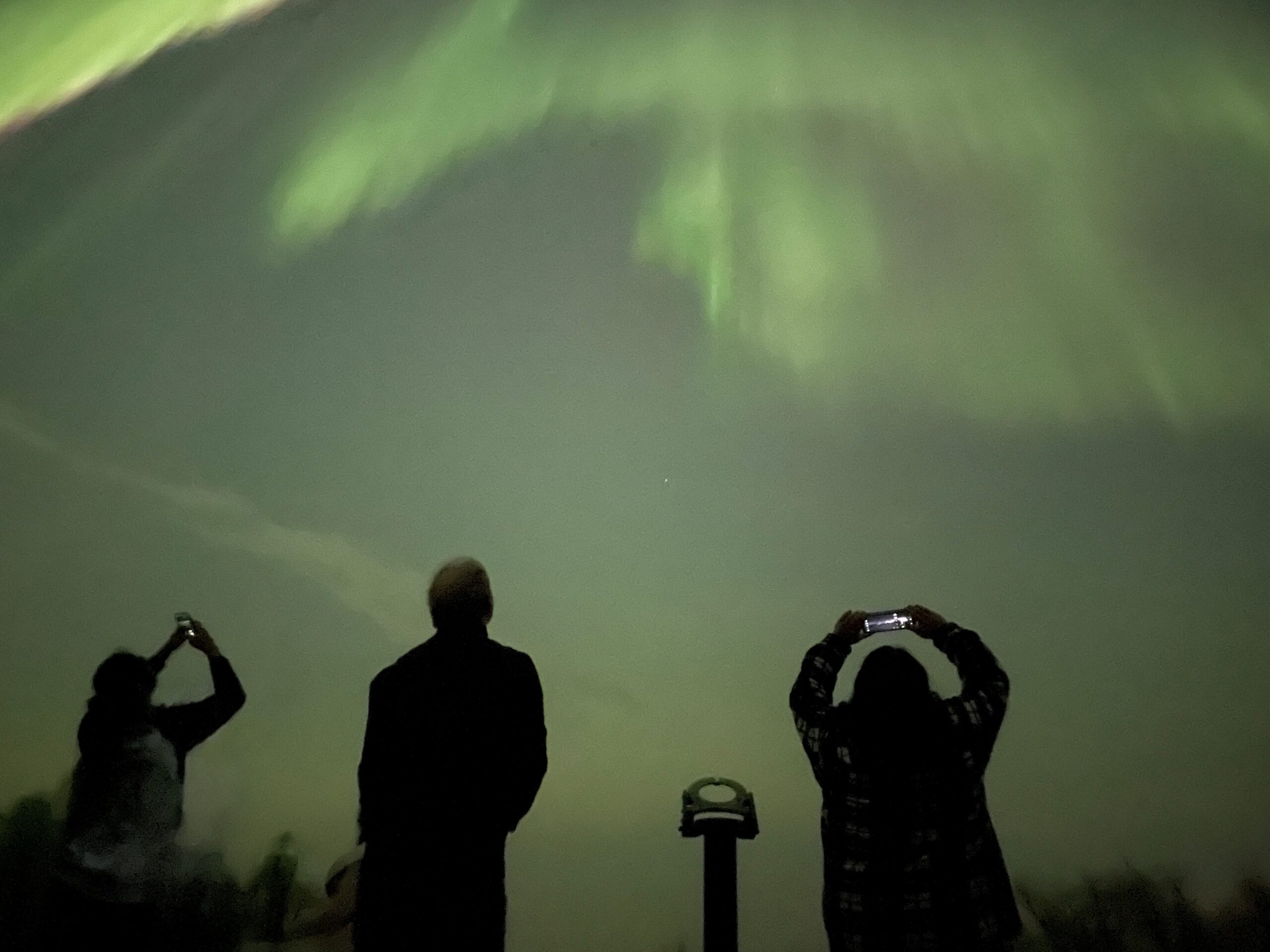 People stare up at the northern lights above them.