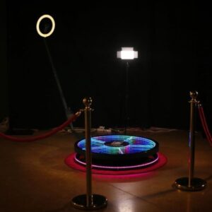 A 360 degree photobooth set up for pictures. An illuminated round platform with a rotating ring light and camera mount.