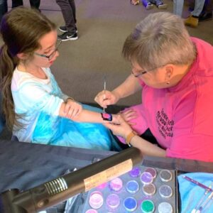 An artist airbrush painting a design on a child's arm.