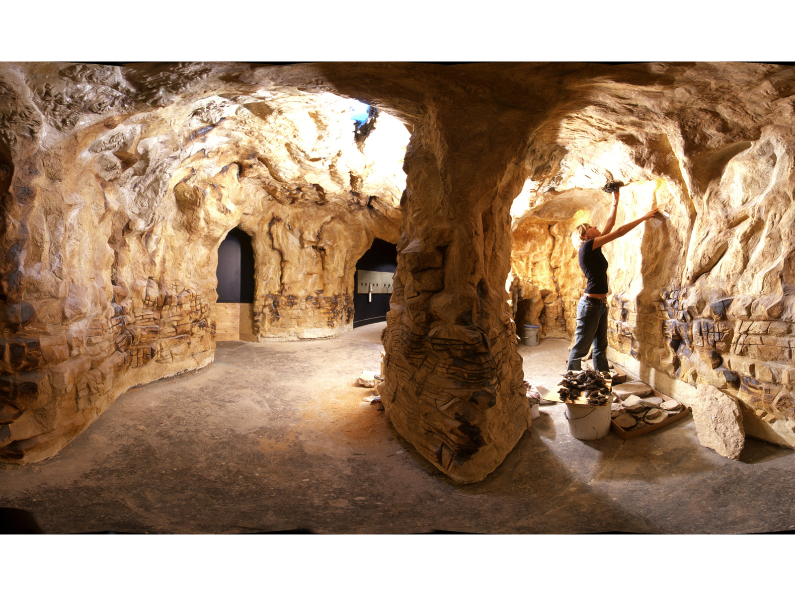 A panoramic view of a recreation of a bat cave, with an individual on the right side of frame placing bat specimens.