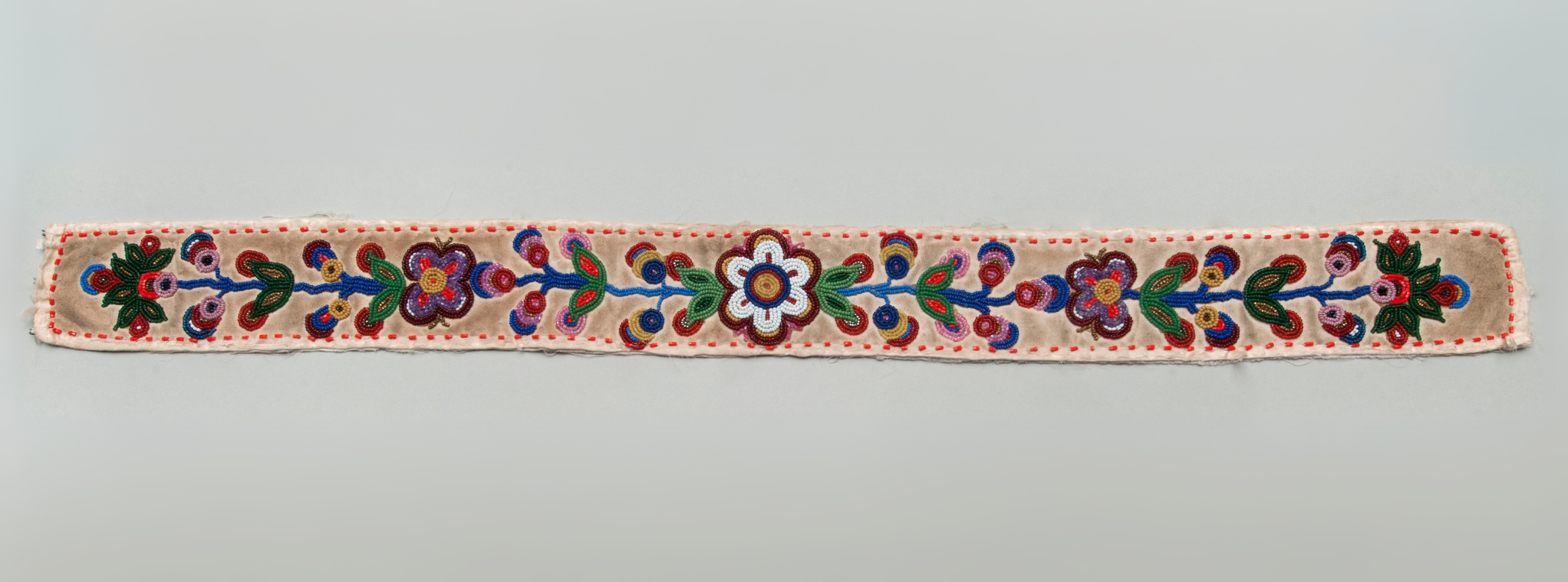 A long thing piece of beadwork with symmetrical floral patterns weaving out from the centre.