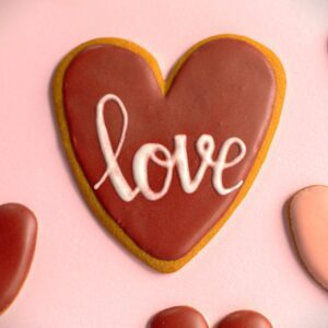 A heart-shaped cookie with red-brown royal icing and the word "love" piped on top.