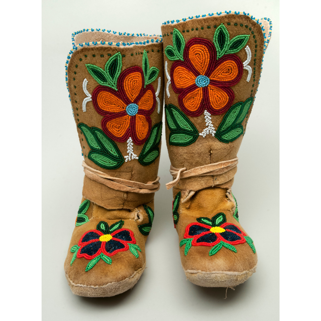 A pair of mid-calf high moccasins with floral beadwork. On the shin of the boot are orange flowers with green leaves, and on the top of the foot are red and black flowers with green leaves.