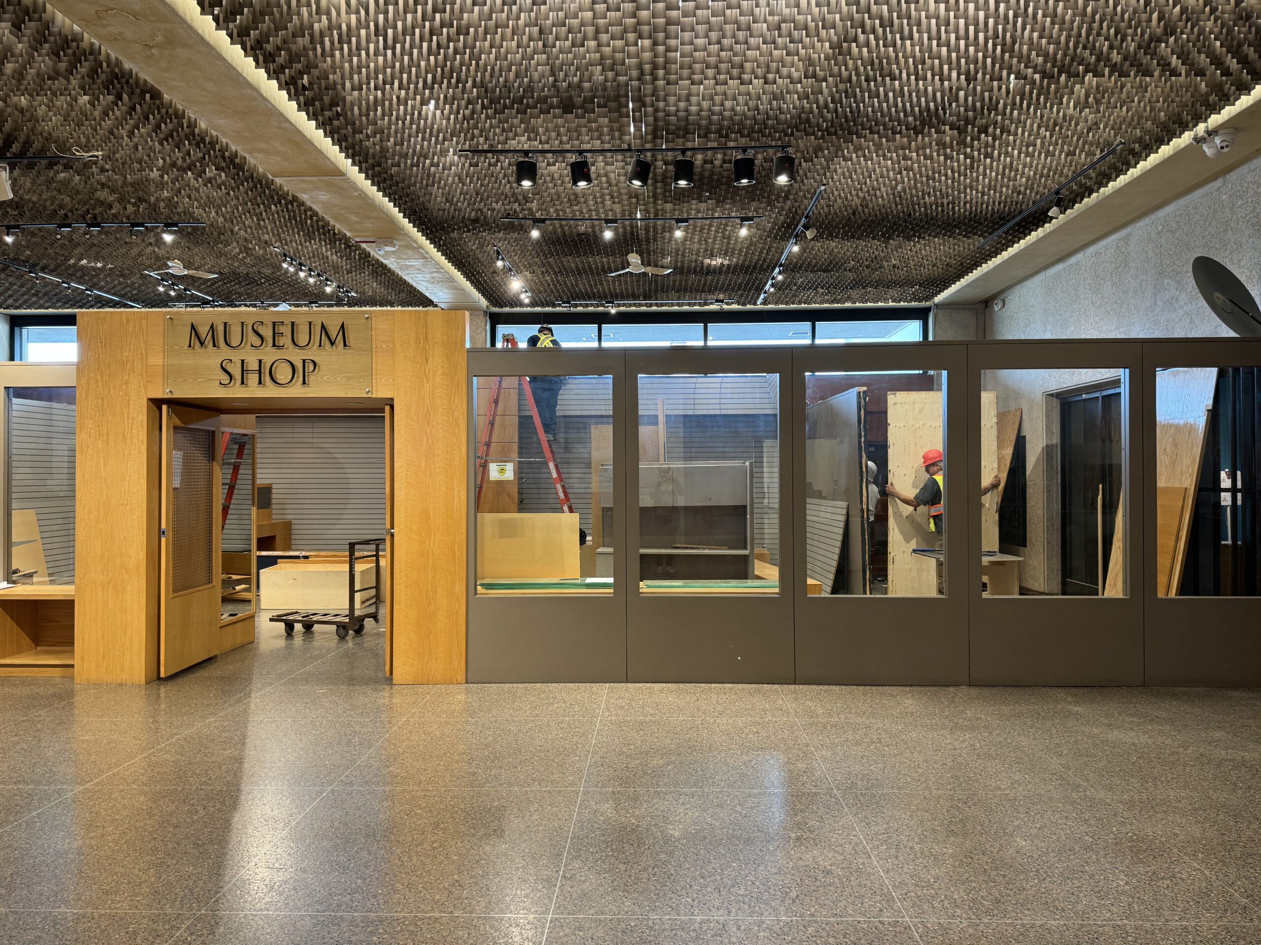 The Museum Shop in the Foyer, with construction workers moving about inside, removing shelves and walls as construction begins.