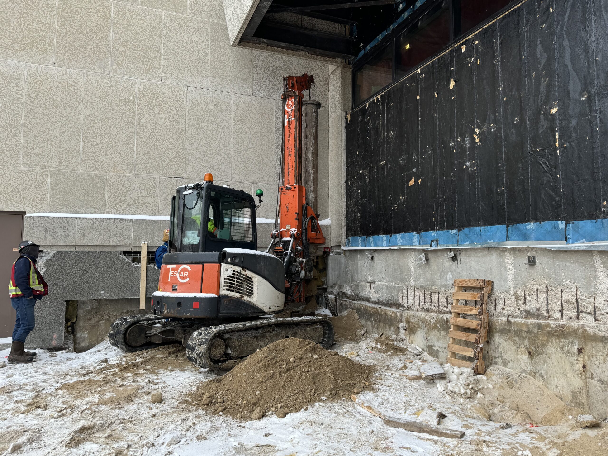 An excavator driving in a pile along the exterior wall of the Museum.