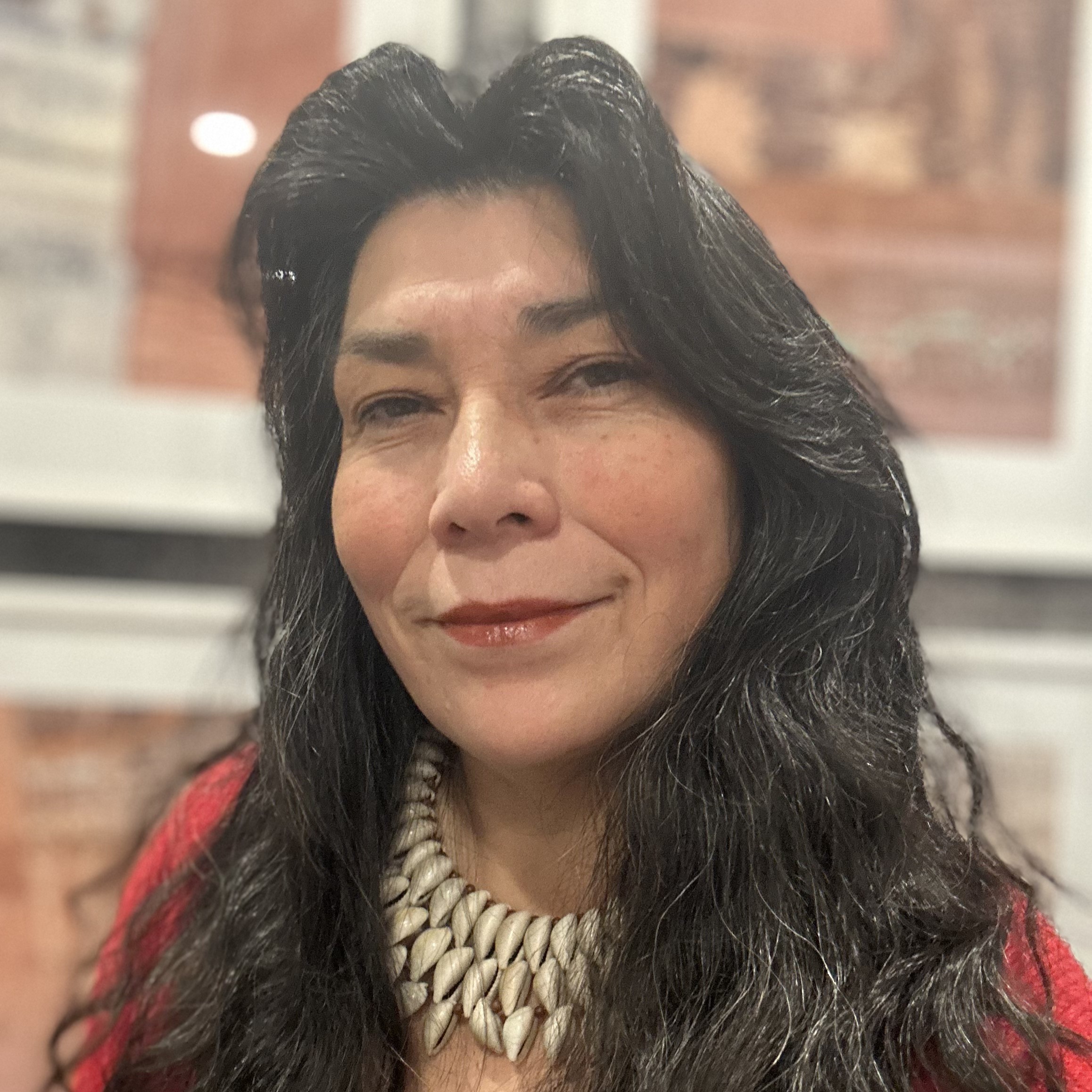 An informal headshot of a smiling woman with long dark hair and wearing a multi-layers shell necklace.