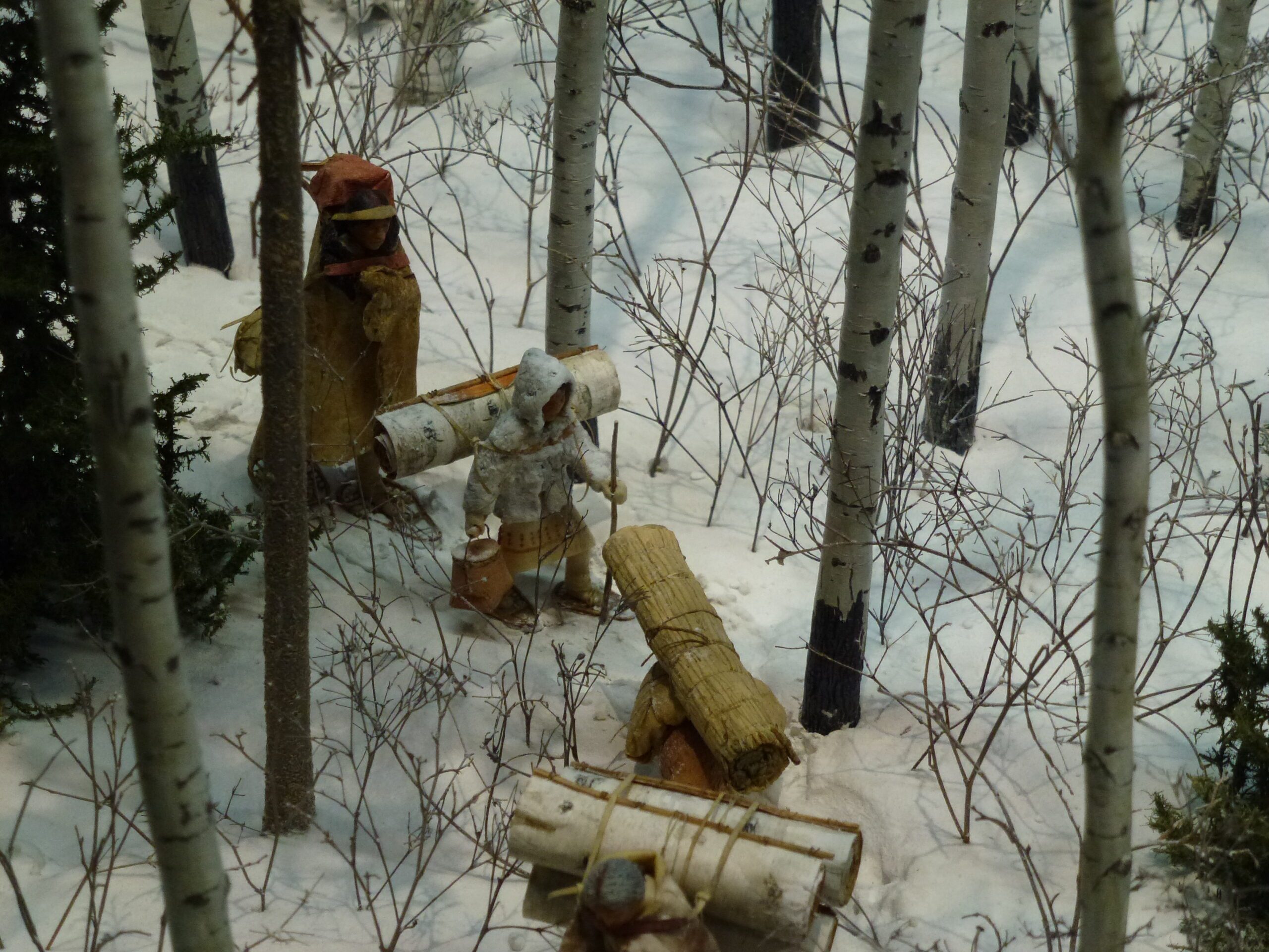 A child figure in a miniature diorama winter scene, wearing traditional winter gear of woven rabbit fur.