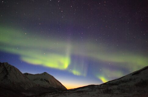 Green northern lights streaking across a night sky over mountain tops.