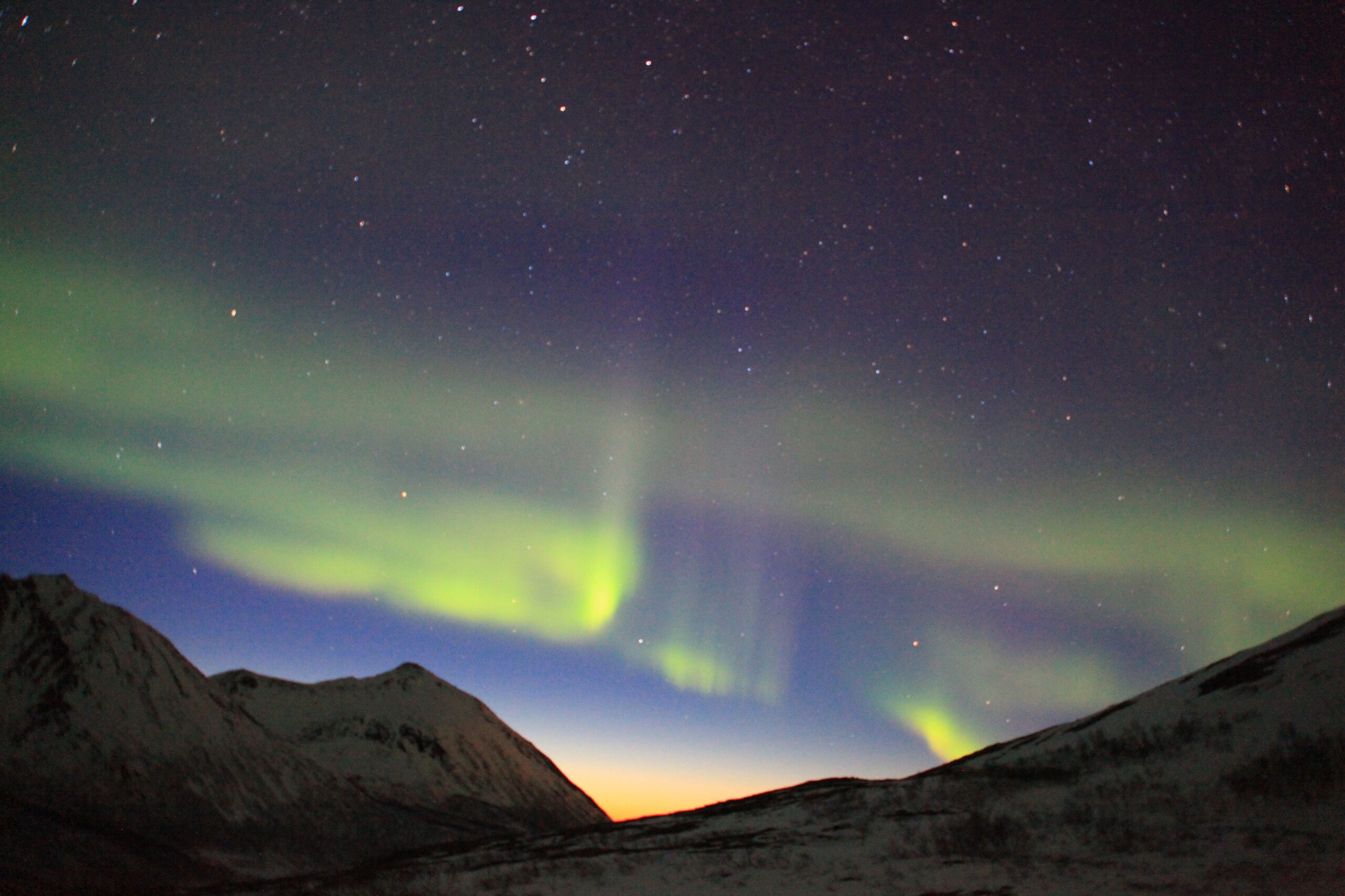 Green northern lights streaking across a night sky over mountain tops.