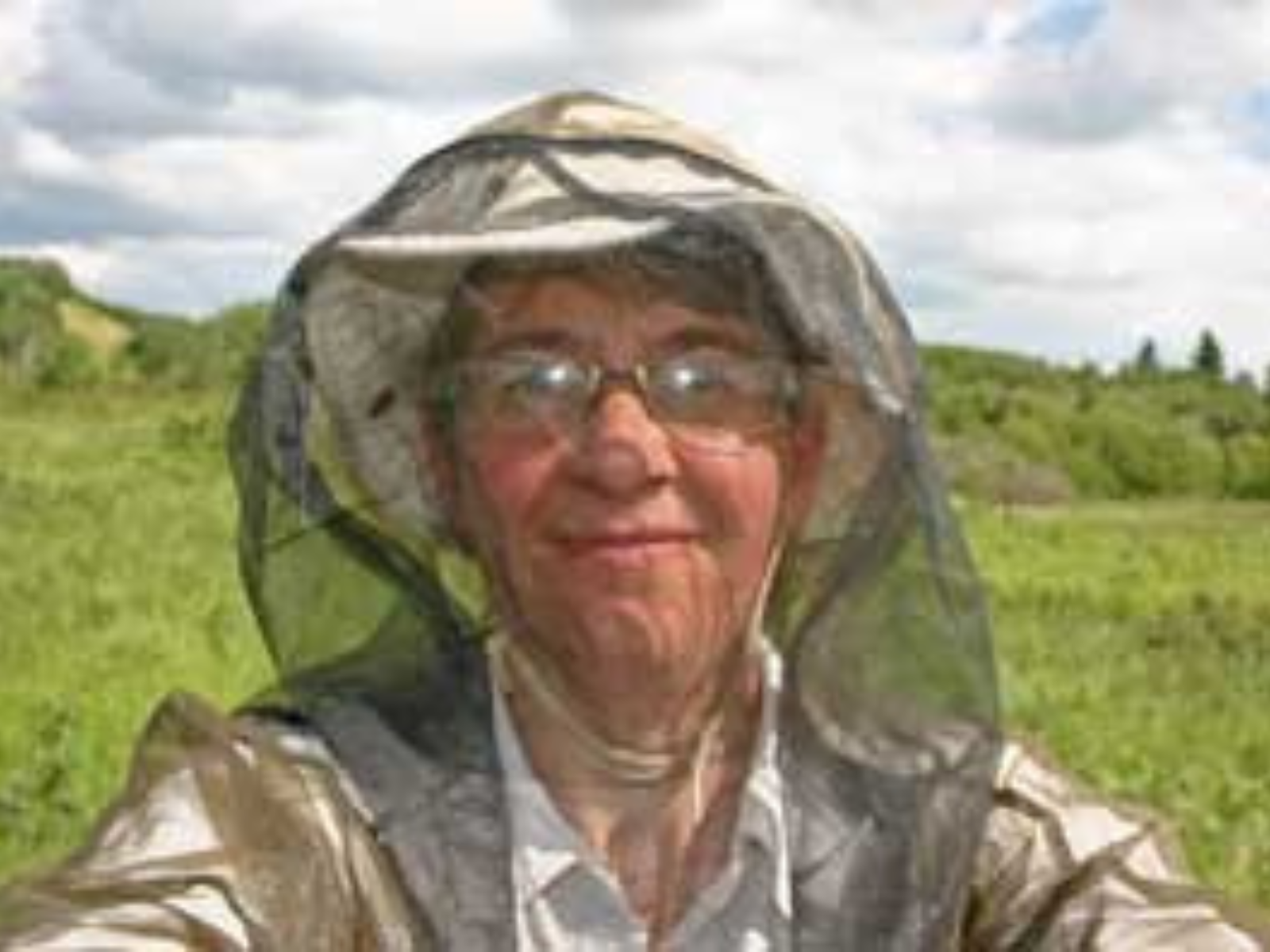 A selfie of a smiling Dr. Diana Bizecki Robson in the field, wearing light coloured clothing and sun hat, zipped into a mosquito jacket with a fully-enclosed hood.