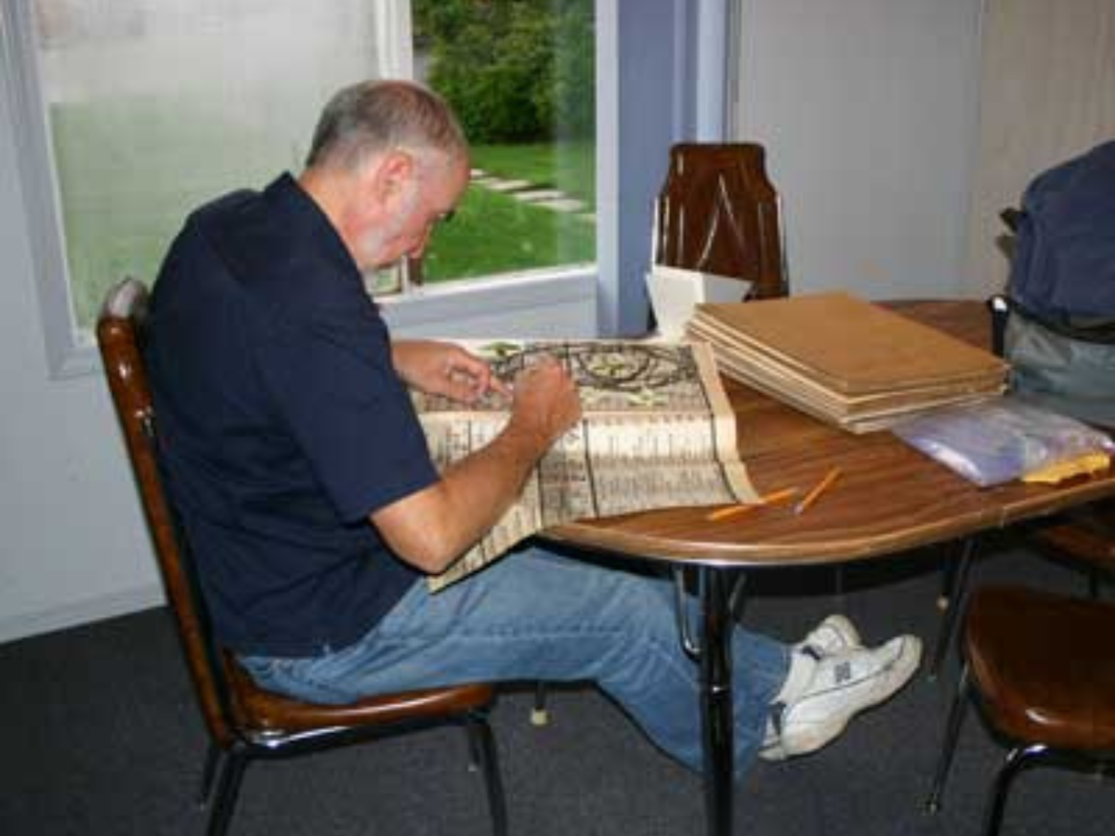 An individual seated at a table placing botany specimens in newspaper for pressing.