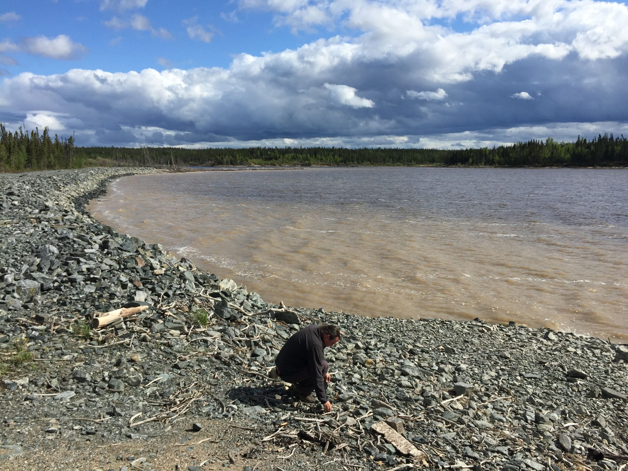 An individual crouched down on a rocky shoreline.