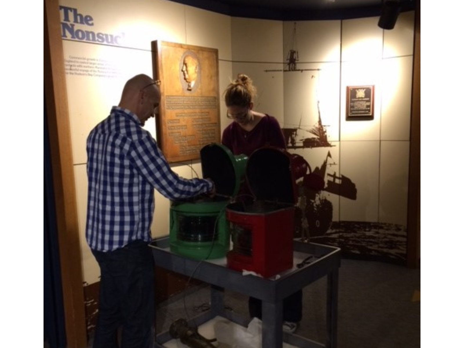 Two individuals either side of a wheeled cart prepping two large ships lanterns for display.