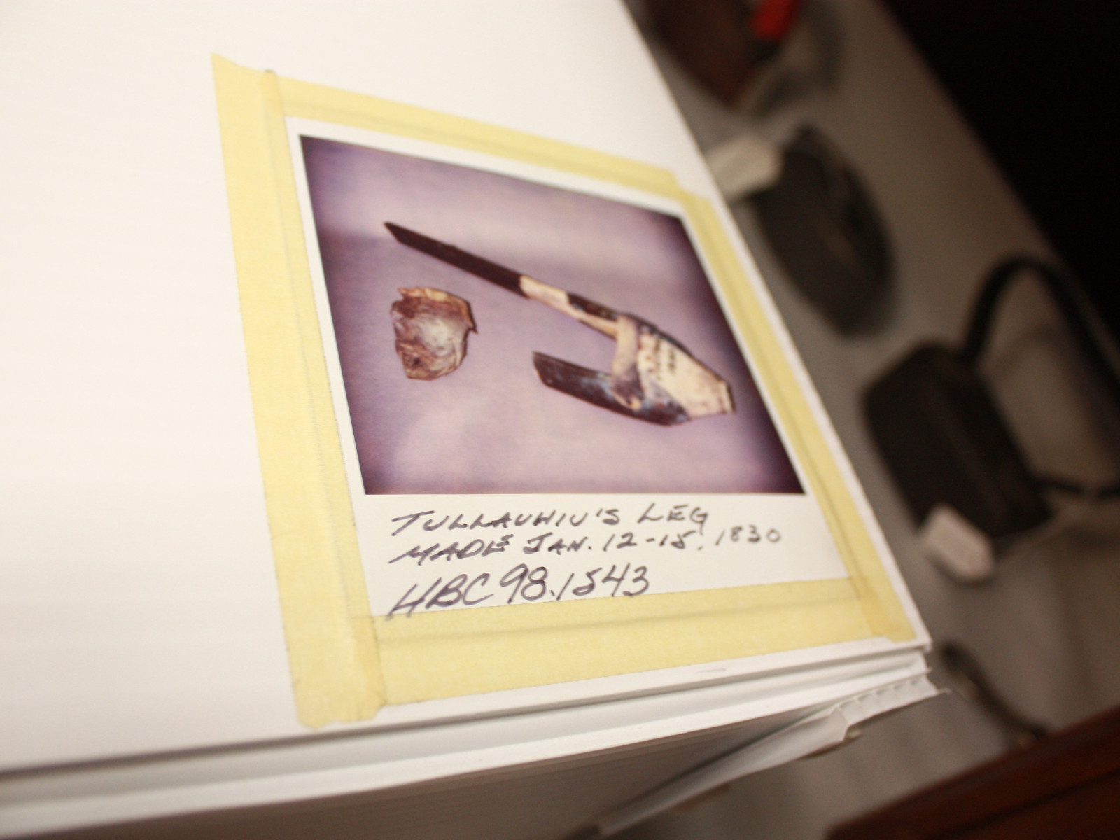 A photograph taped to the top of a collections storage box showing a rudimentary prosthesis leg, labelled "Tullauhiu's leg".