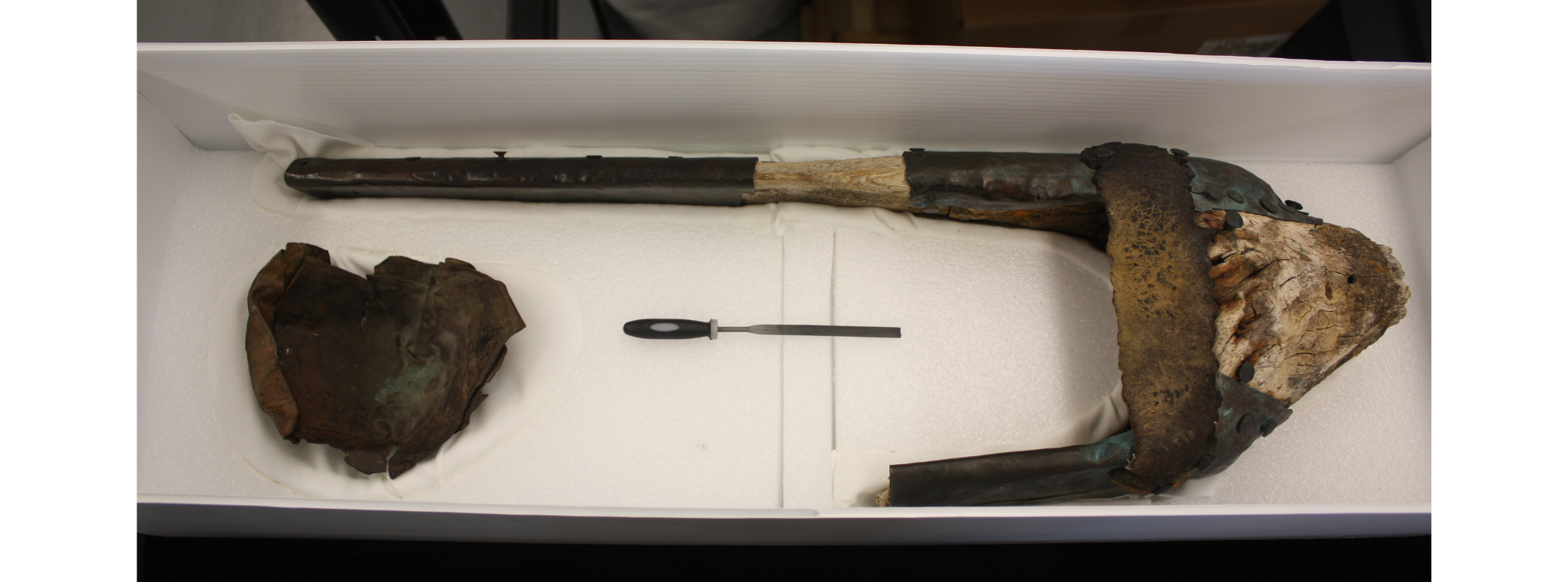 A rudimentary wooden prosthetic leg in an open collections storage box.