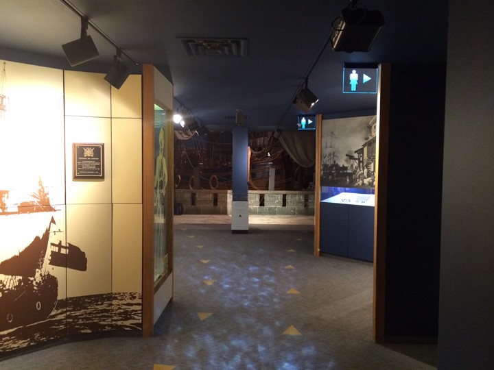 Looking down a weaving hallway with two rows of arrows directing visitors both down and up the hallway. Lighting casts a blue glow on the main walk way, and illuminated signs direct visitors in the directions of the washrooms.