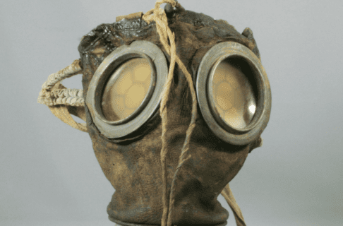 A gas mask with large screened eye windows and a tubular breathing vent.