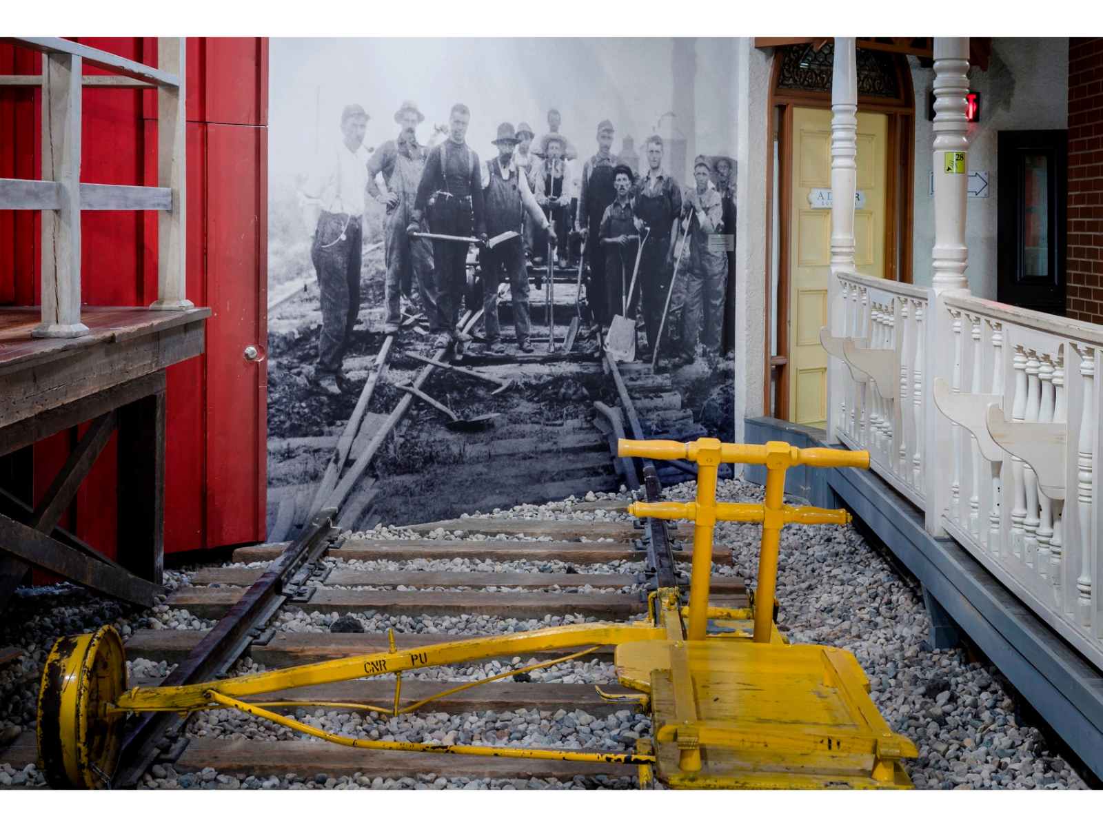 A historical photograph blown up on the wall showing a railway worked gang standing around a railway line. The photograph lines up with a railway line built our in the Winnipeg 1920 Cityscape.