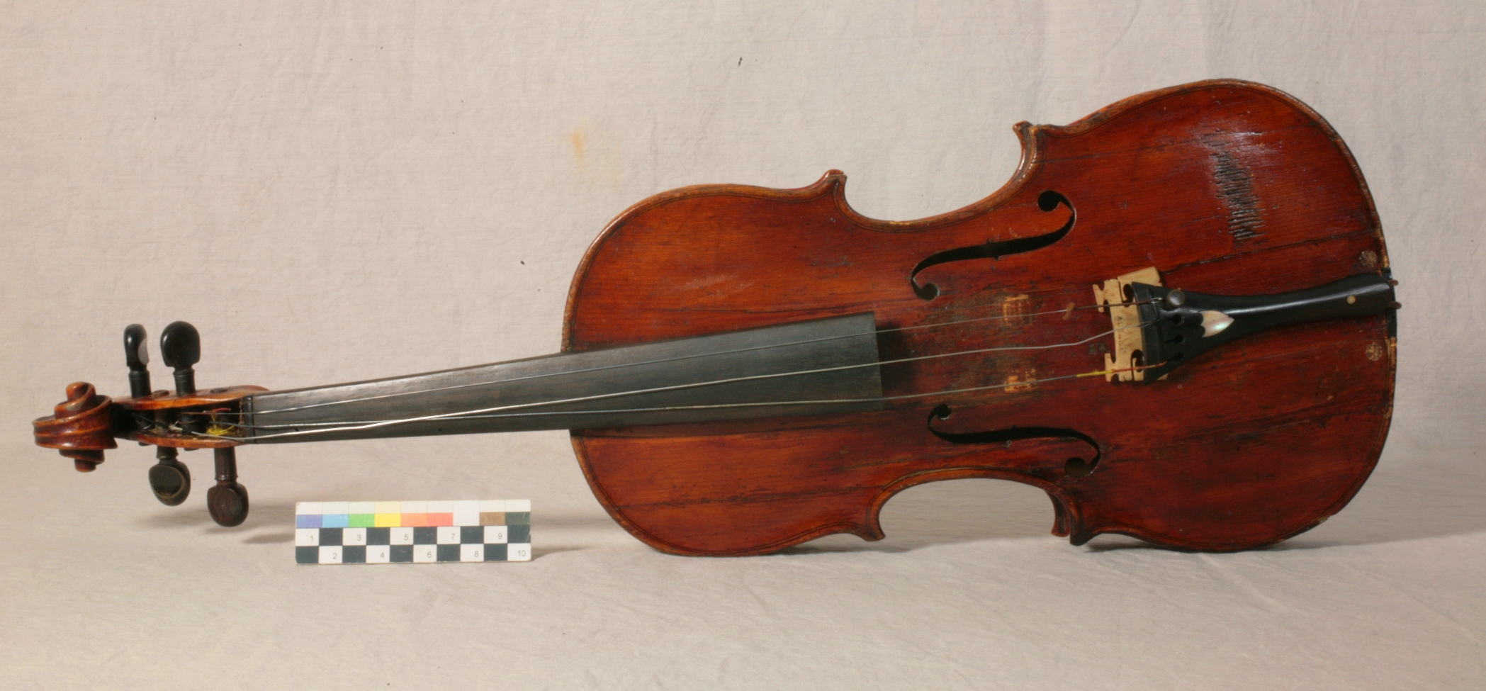 A violin with loose strings laid on its side against a cream coloured background.