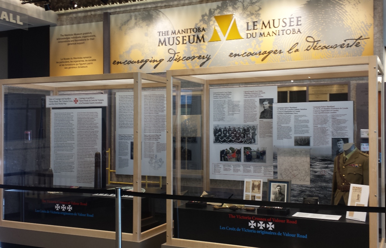 Two display cases with artifacts and text panels under a large Manitoba Museum banner.