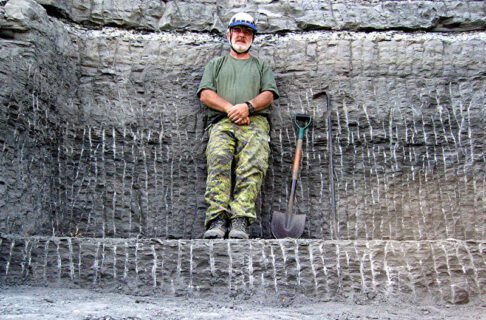 An individual standing on a stone shelf against a stone wall next to a shovel and pick tool.