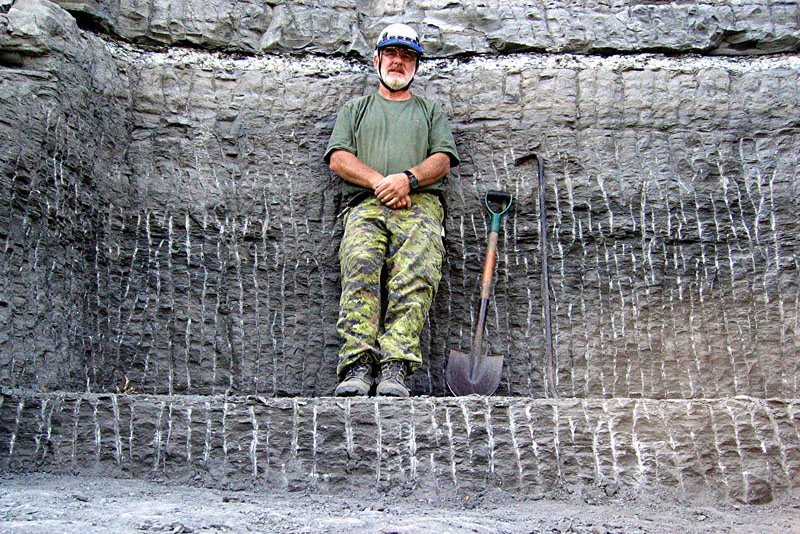 An individual standing on a stone shelf against a stone wall next to a shovel and pick tool.