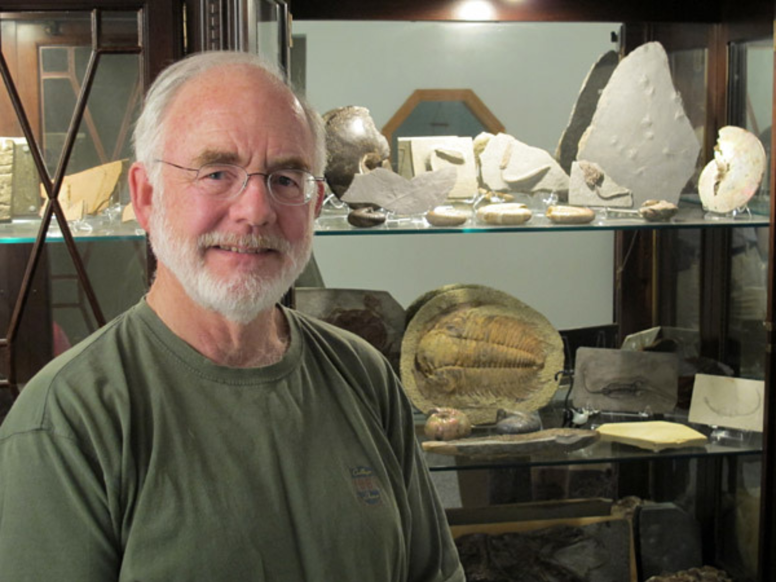 A smiling individual standing in front of a display cabinet filled with fossil specimens.