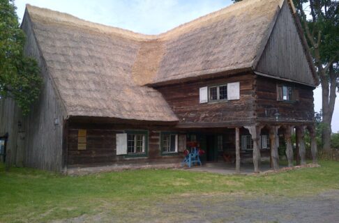 A large building with a thatched roof. The second storey extends from the centre of the lower storey creating a sheltered overhang.