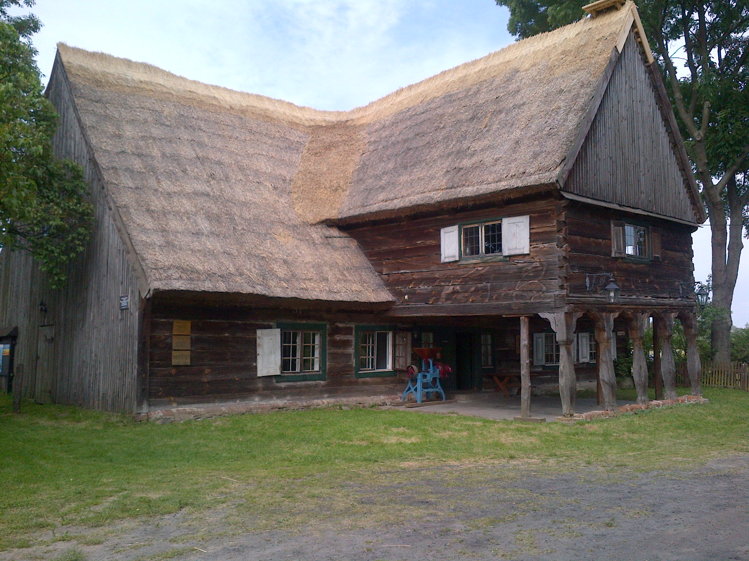 A large building with a thatched roof. The second storey extends from the centre of the lower storey creating a sheltered overhang.