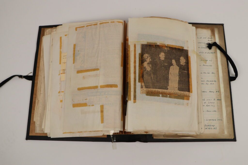 Large scrapbook with pieces of old tape attached to the pages and a newspaper clipping on the right page.