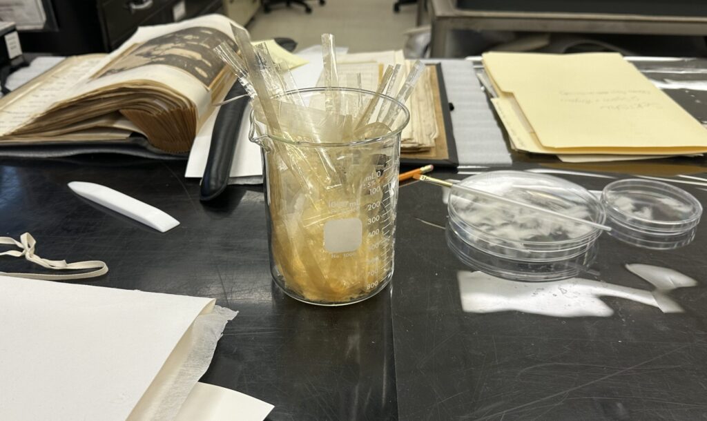 Beaker filled with translucent cellulose tape with an opened scrapbook sitting behind the beaker.