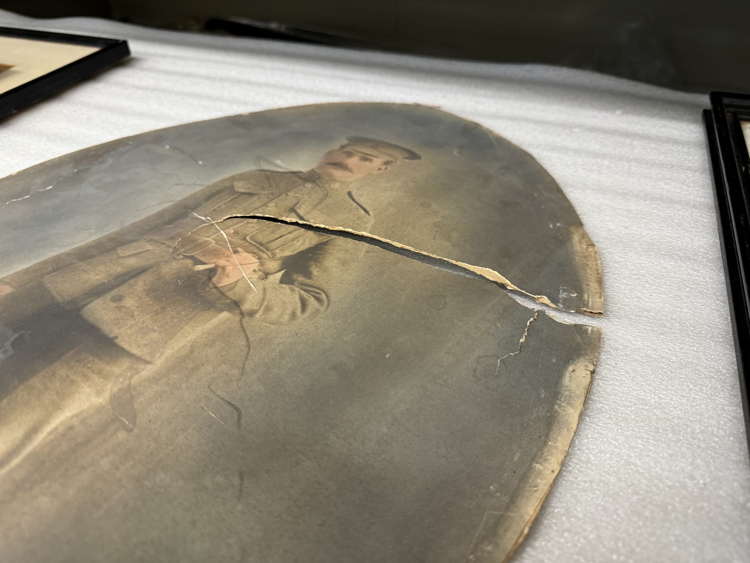 An oval photograph of a soldier in uniform. from one side through to the centre the material the photograph is printed on has been torn. The edges are worn.